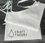 White apron on dark wood background with Craft Theory logo